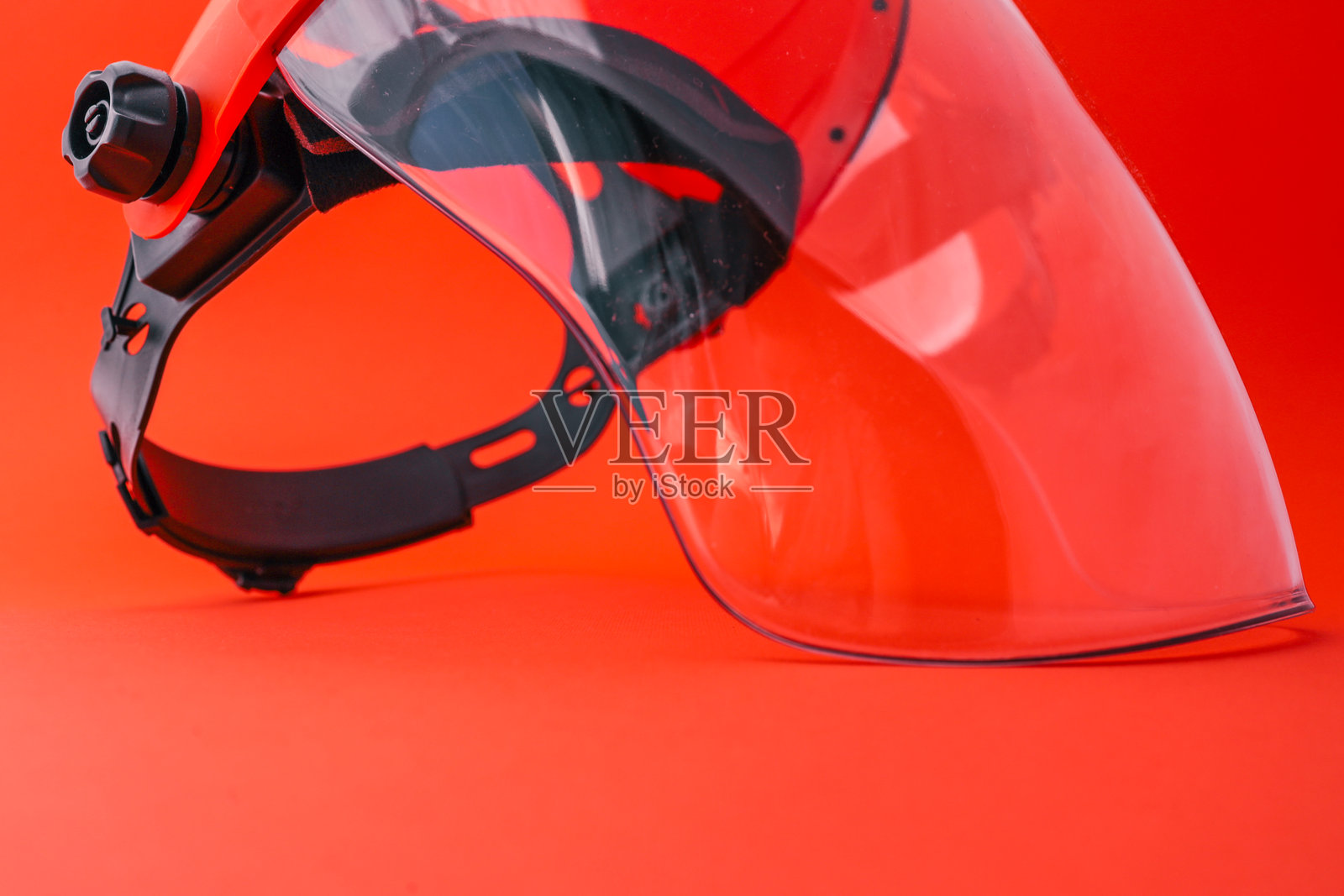 带有透明面罩和橙色头盔的防护面罩，孤立在明亮的红色背景上，用于工业、建筑或园艺工作的安全防护照片摄影图片