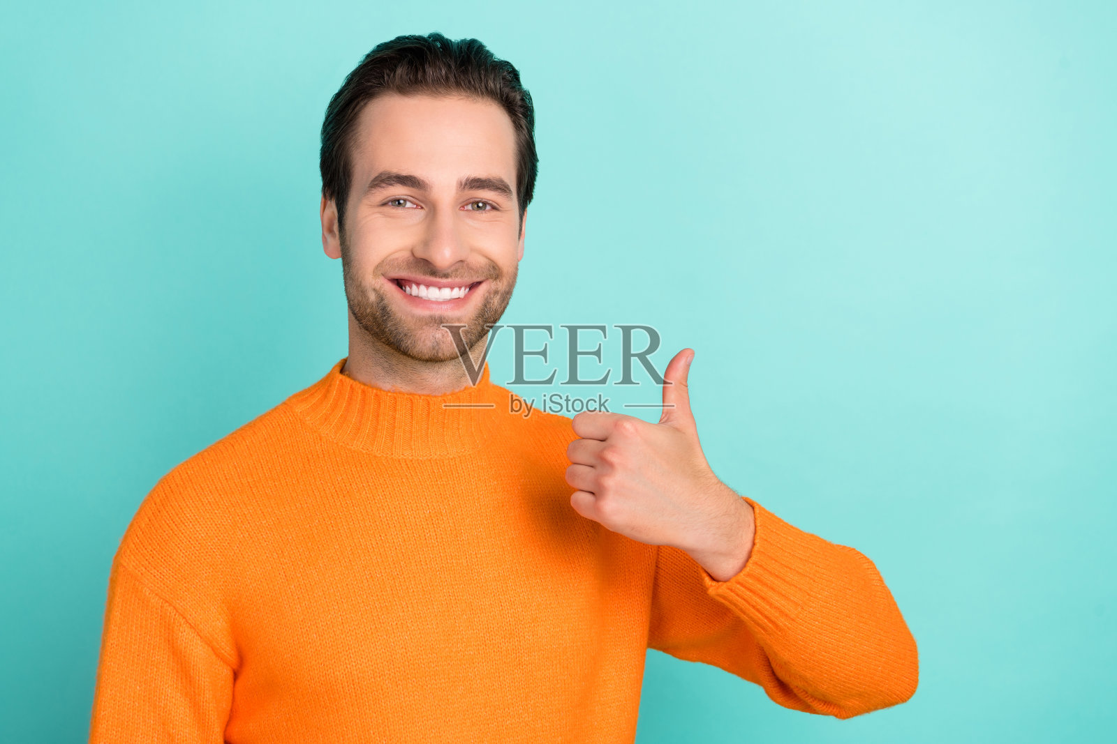 年轻男子竖起大拇指表示赞同，选择推广者，背景为青色。照片摄影图片