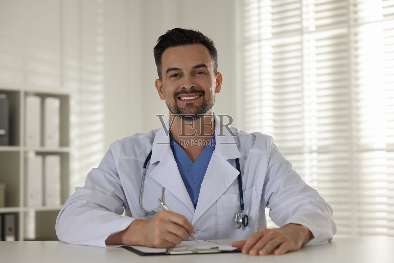 微笑的医生在诊所的桌子旁拿着夹板照片摄影图片