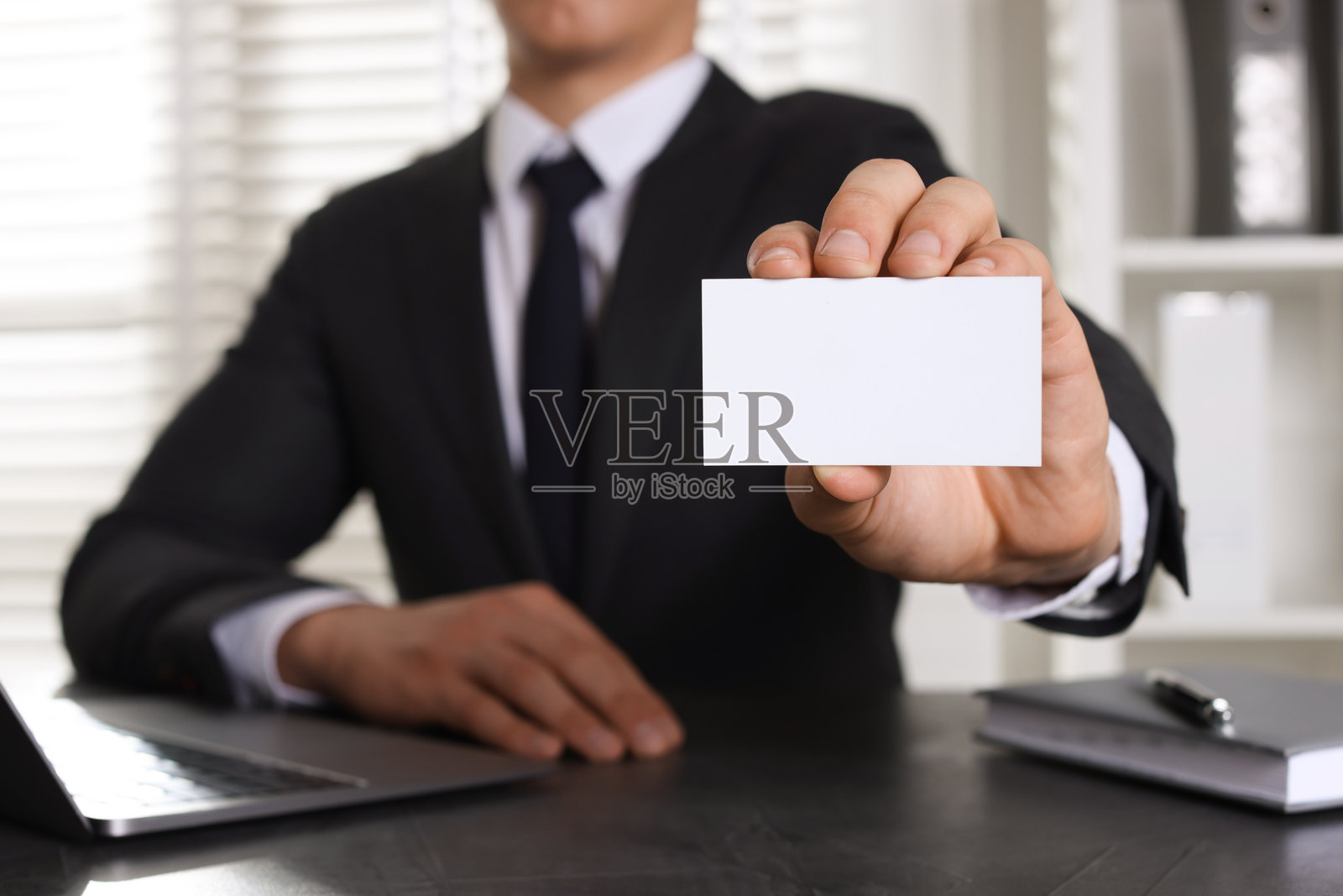 男人在办公室桌子上拿着空白名片，特写。设计的样板。照片摄影图片