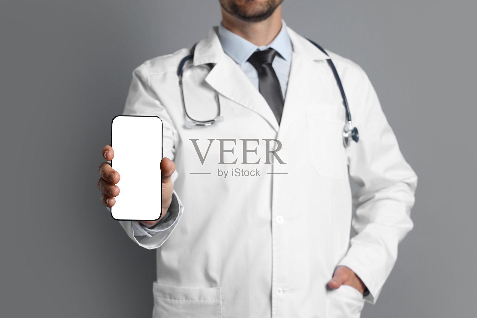 医生在灰色背景下展示一部屏幕空白的智能手机，特写镜头。设计的样板。照片摄影图片