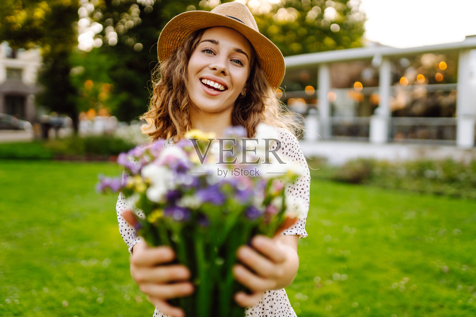一位美丽的女性手持手机，手捧一束郁郁葱葱的野花，在绿色公园中享受日落。照片摄影图片