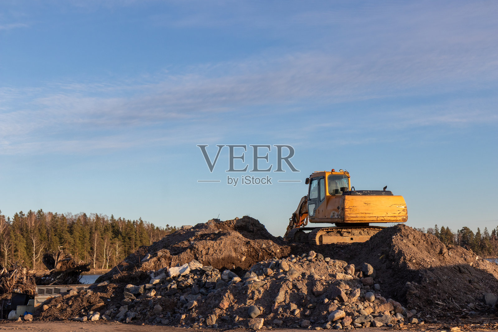 黄昏时分的黄色挖掘机在施工现场进行土方作业，蓝天上的挖掘机。重型施工设备在施工现场进行挖掘，露天采矿。照片摄影图片