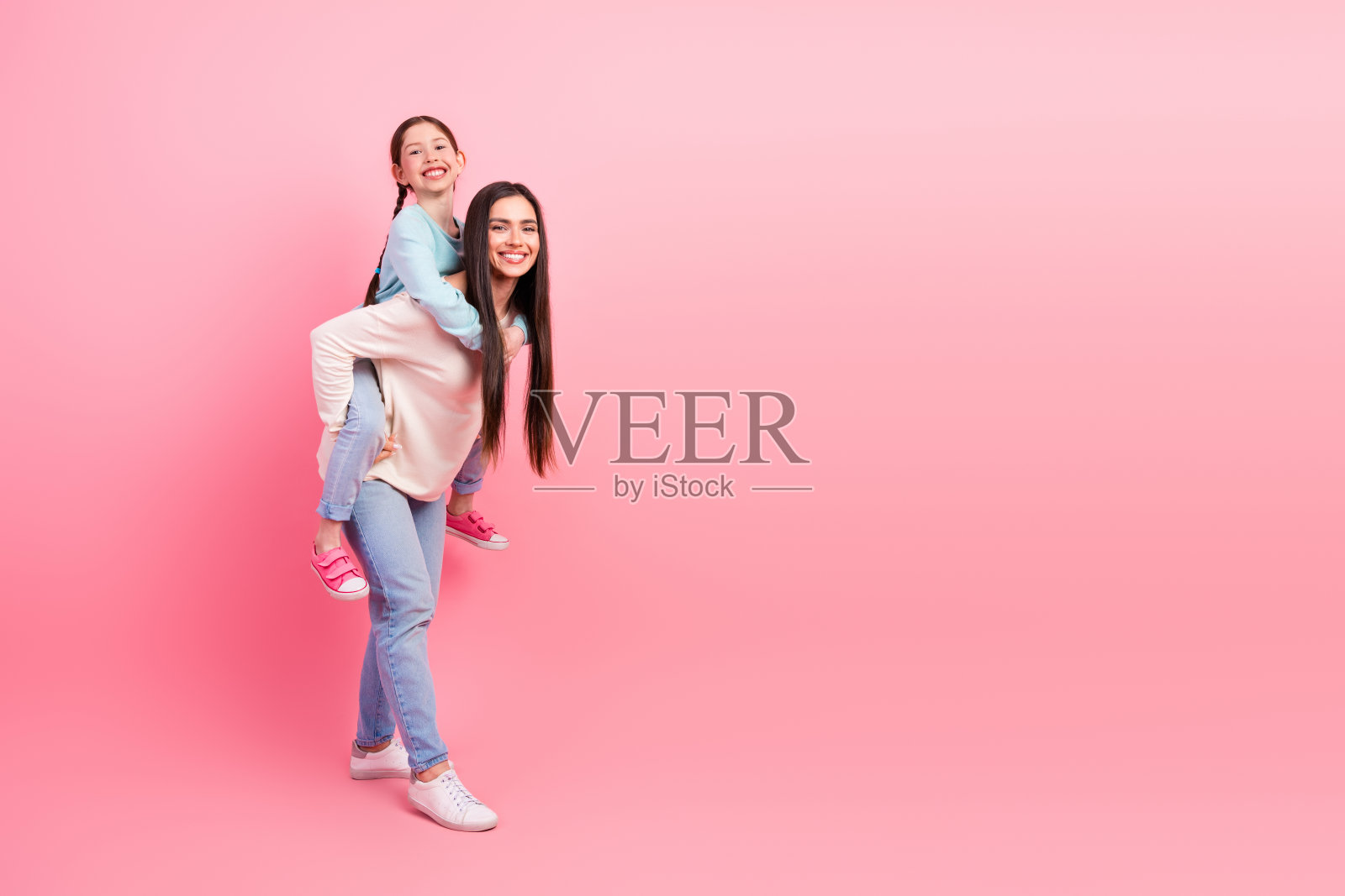 母女在鲜艳的粉色背景下享受高质量的亲密时光，表达着快乐、青春和时尚。照片摄影图片