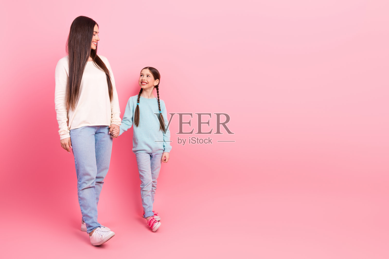 母女牵手，在明亮的粉色背景下享受愉快的时刻照片摄影图片