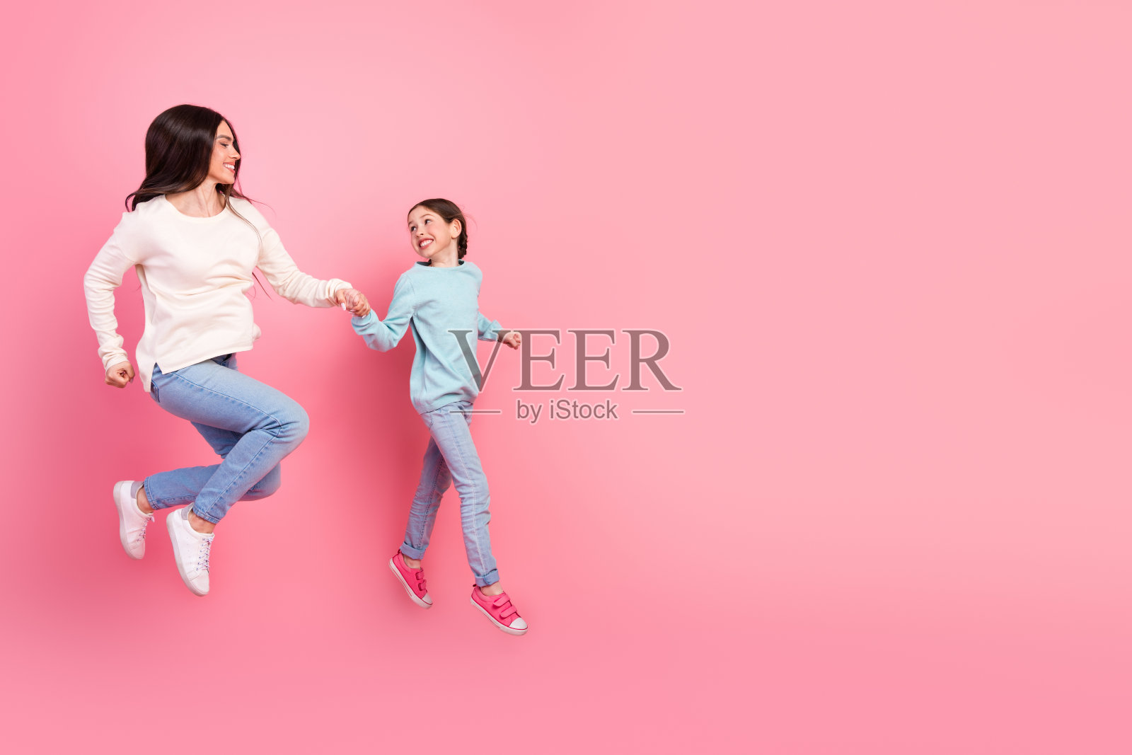 母女俩穿着休闲服装，在明亮的粉色背景下欢笑跳跃，享受美好时光。照片摄影图片