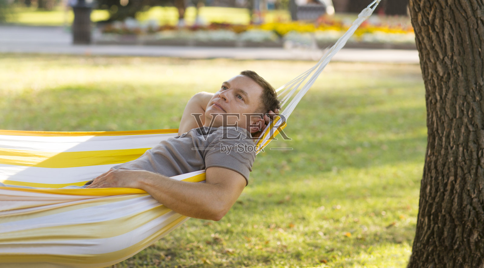 成熟微笑的男人躺在花园的秋千椅上，夏日阳光下注视着镜头。照片摄影图片