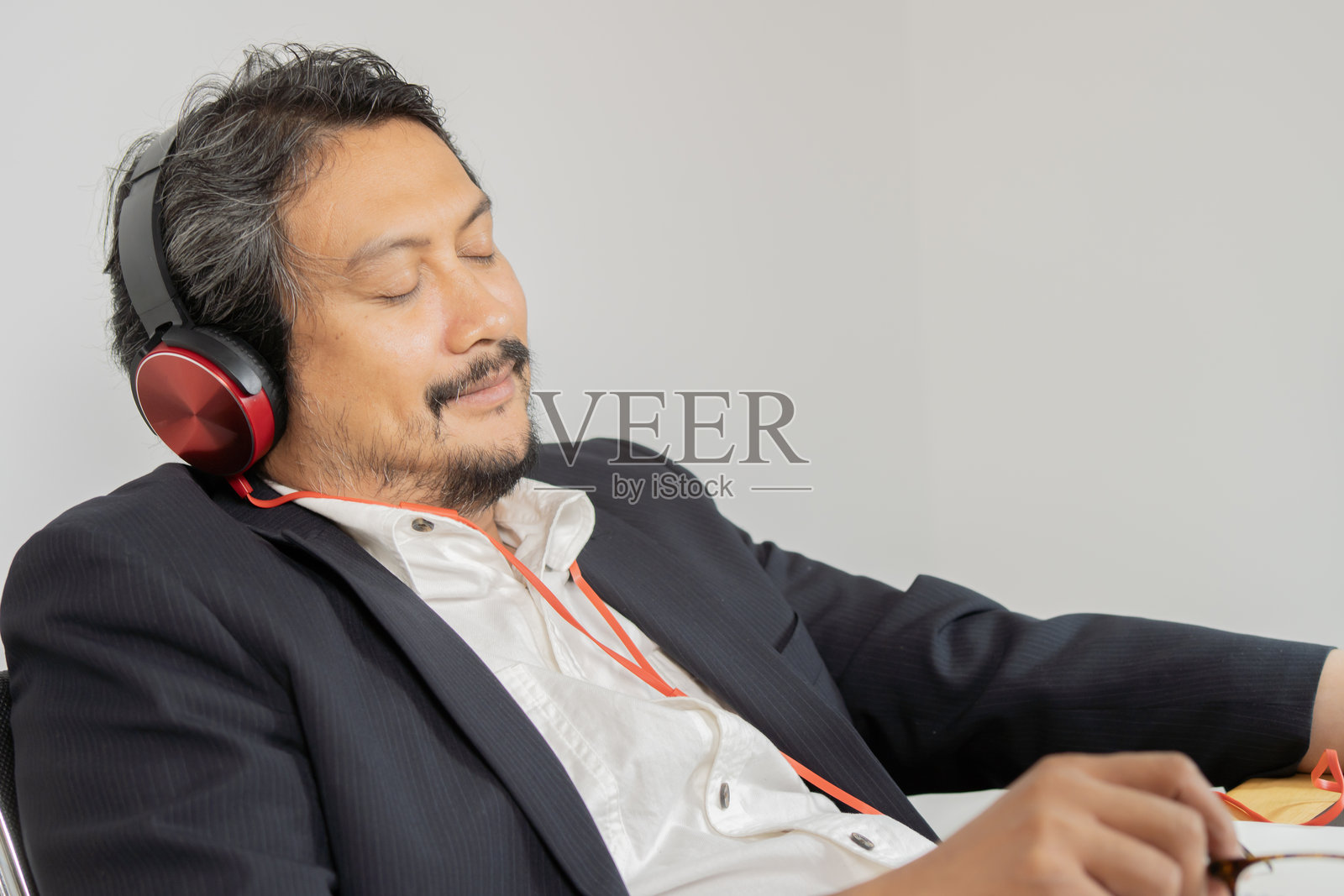 商人在办公室里戴着耳机休息，听音乐和有声书播客照片摄影图片