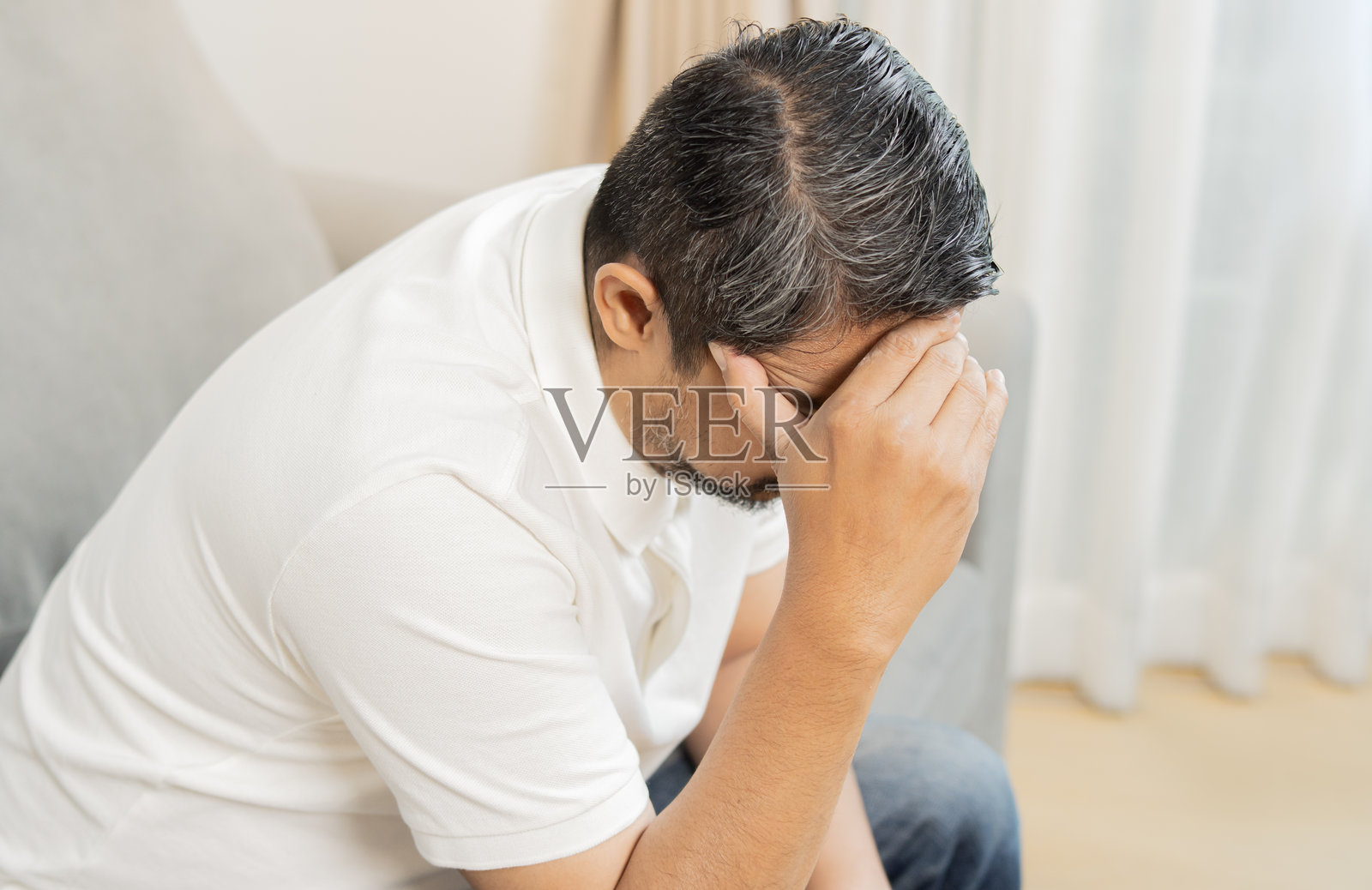 高角度视图的成熟男性坐在家中，靠近门，手放在头上。照片摄影图片