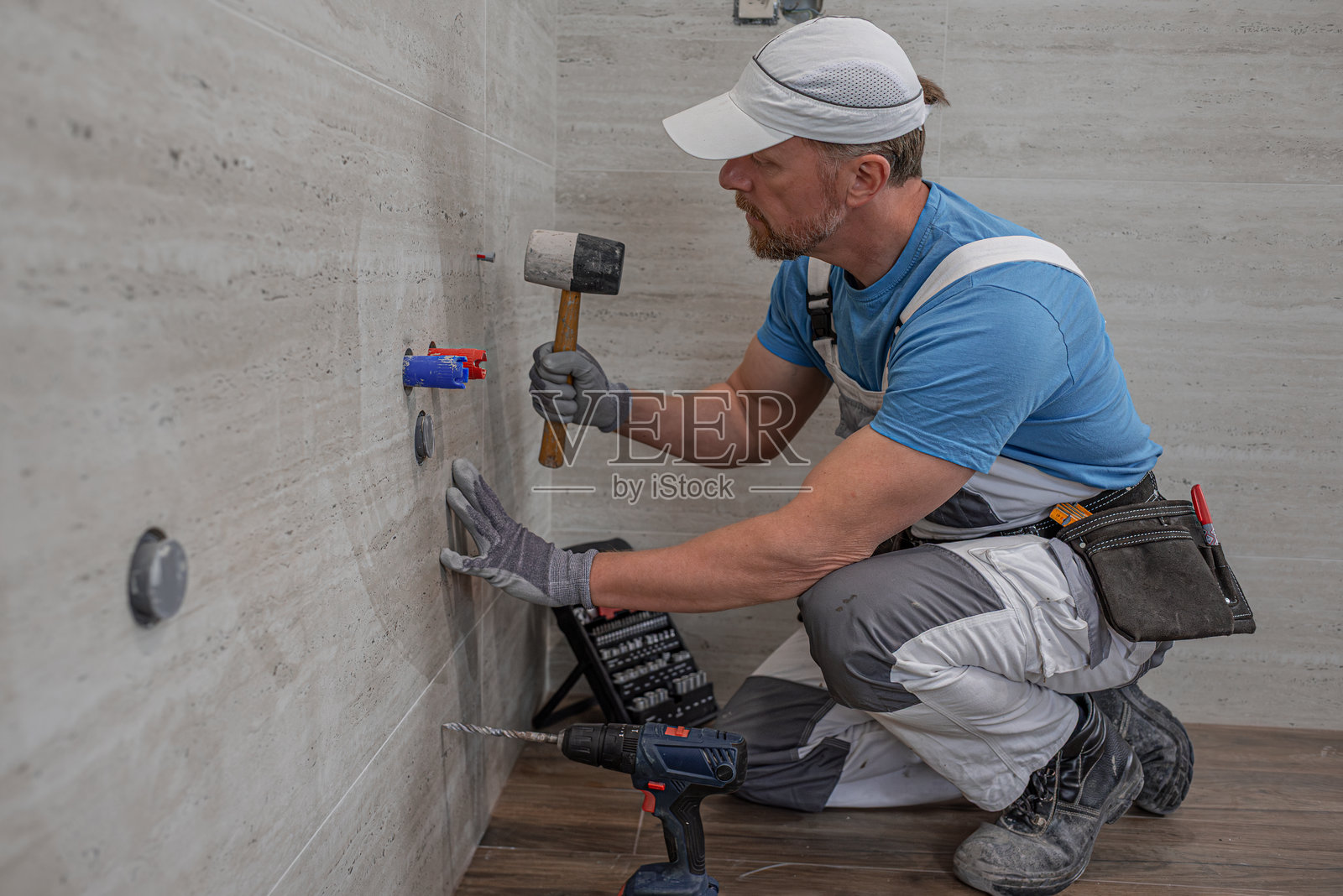 安装浴室家具。水管工正在将膨胀螺丝锤入孔中。照片摄影图片