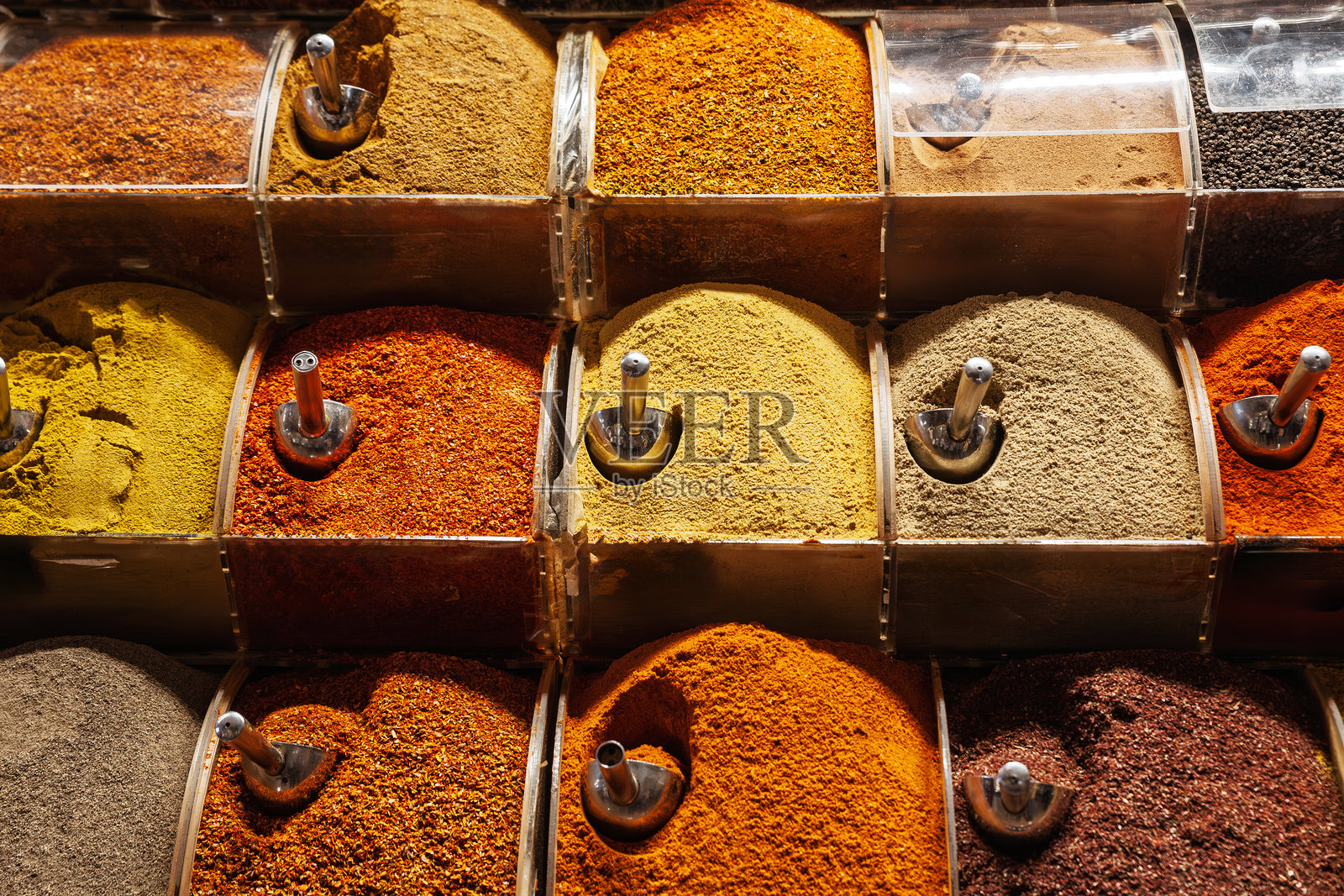 伊斯坦布尔的米斯尔市场（Misir Carsisi）中五彩缤纷的磨碎香料，温暖的光线突显了丙烯容器中的姜黄、红椒粉、咖喱和孜然堆。照片摄影图片