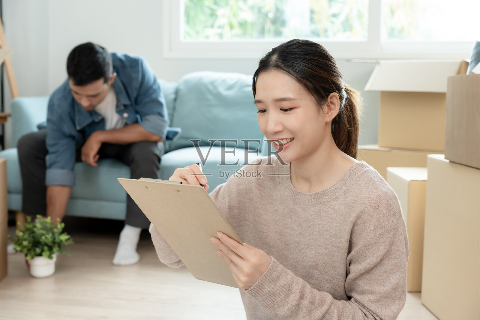 搬家，迁移。妻子正在使用家庭清单为新公寓做准备。房间内有装满个人物品和家具的纸箱。搬入一栋房子或公寓。照片摄影图片