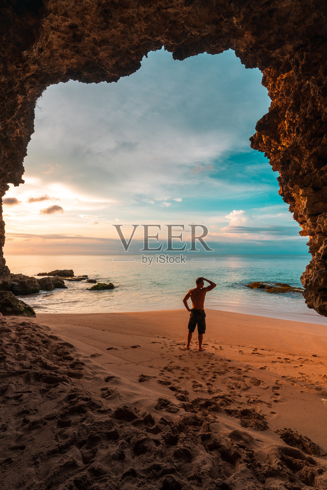 旅行者在热带海滩的山洞中欣赏美丽的景色，背景是湛蓝的天空和清澈的海洋。照片摄影图片