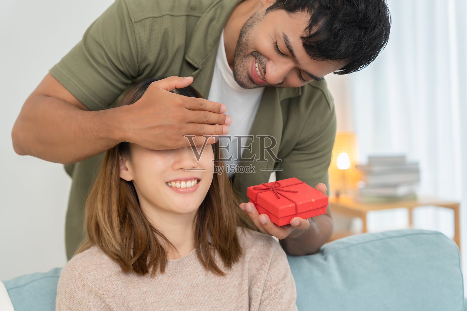 丈夫亲吻妻子的眼睛，给她一个惊喜。可爱的女孩对礼物盒感到兴奋。生日、庆祝、圣诞节、新年节日、感谢、庆祝、情人节、结婚周年。照片摄影图片