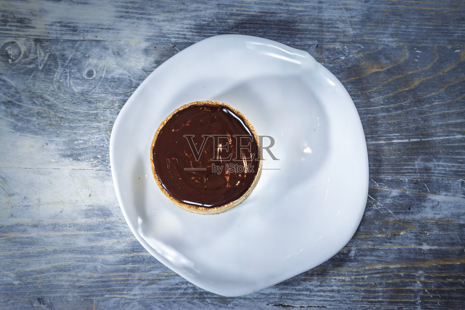 白色盘子上的单个法式巧克力塔，放置在乡村风格的蓝灰色木桌上，称为巧克力塔小点心，它是法式糕点料理的典型代表。照片摄影图片