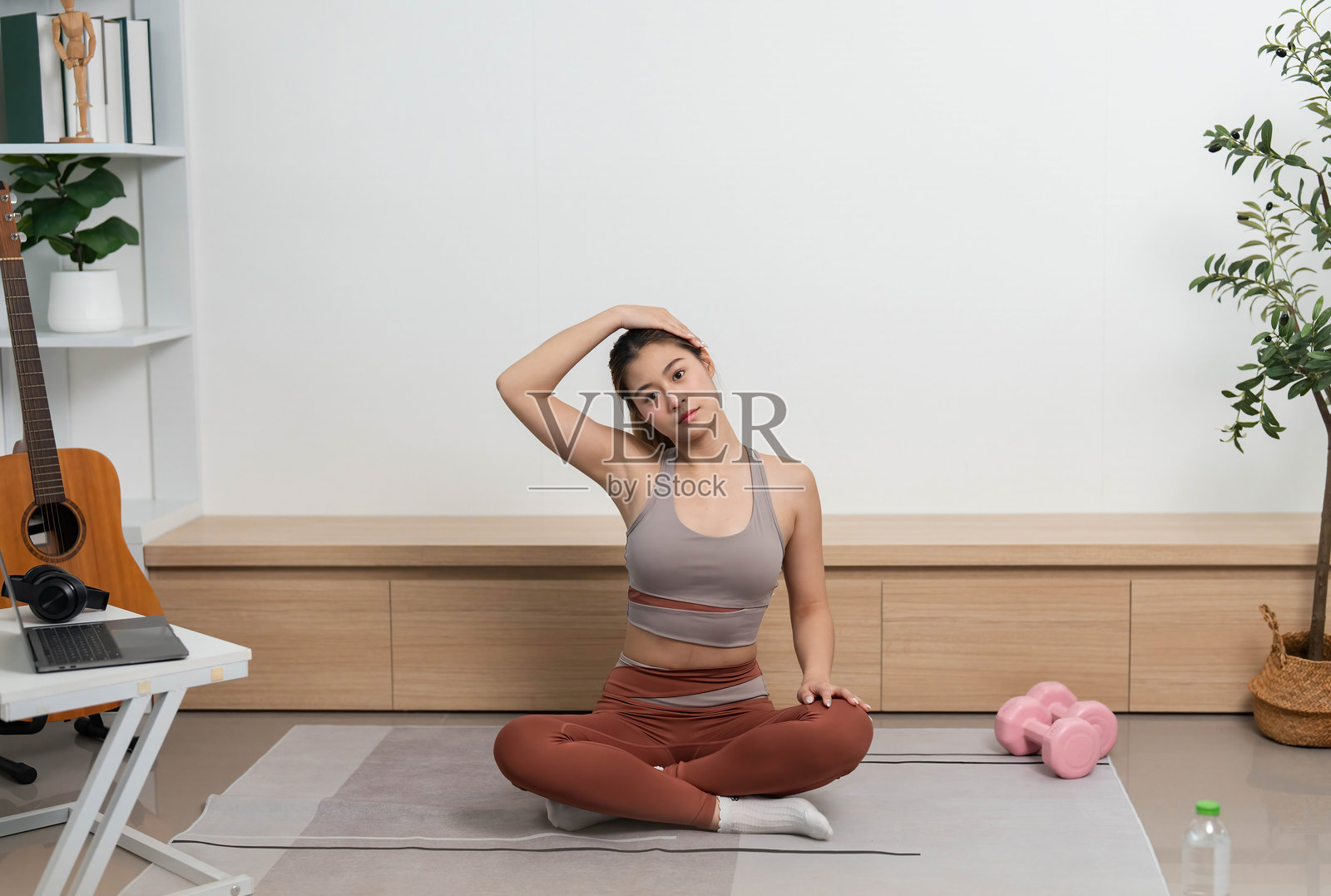 在家进行瑜伽课程。女性在瑜伽垫上做颈部拉伸。照片摄影图片