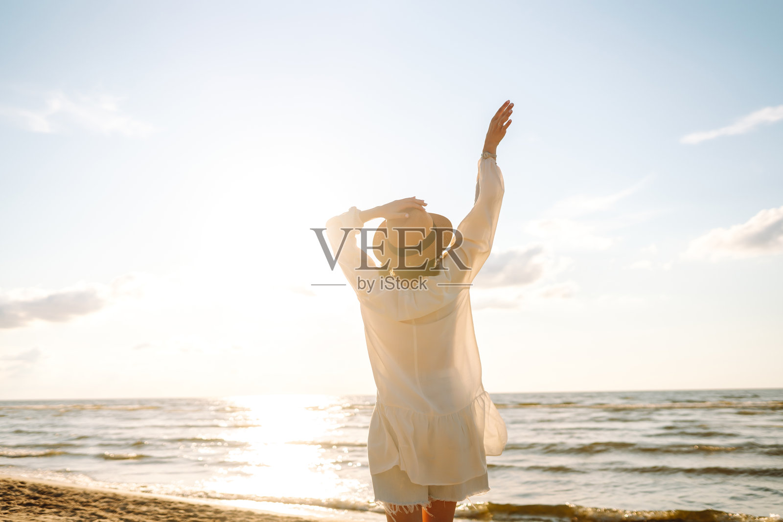 微笑的女性戴着帽子和太阳镜，在阳光明媚的海滩上散步。照片摄影图片