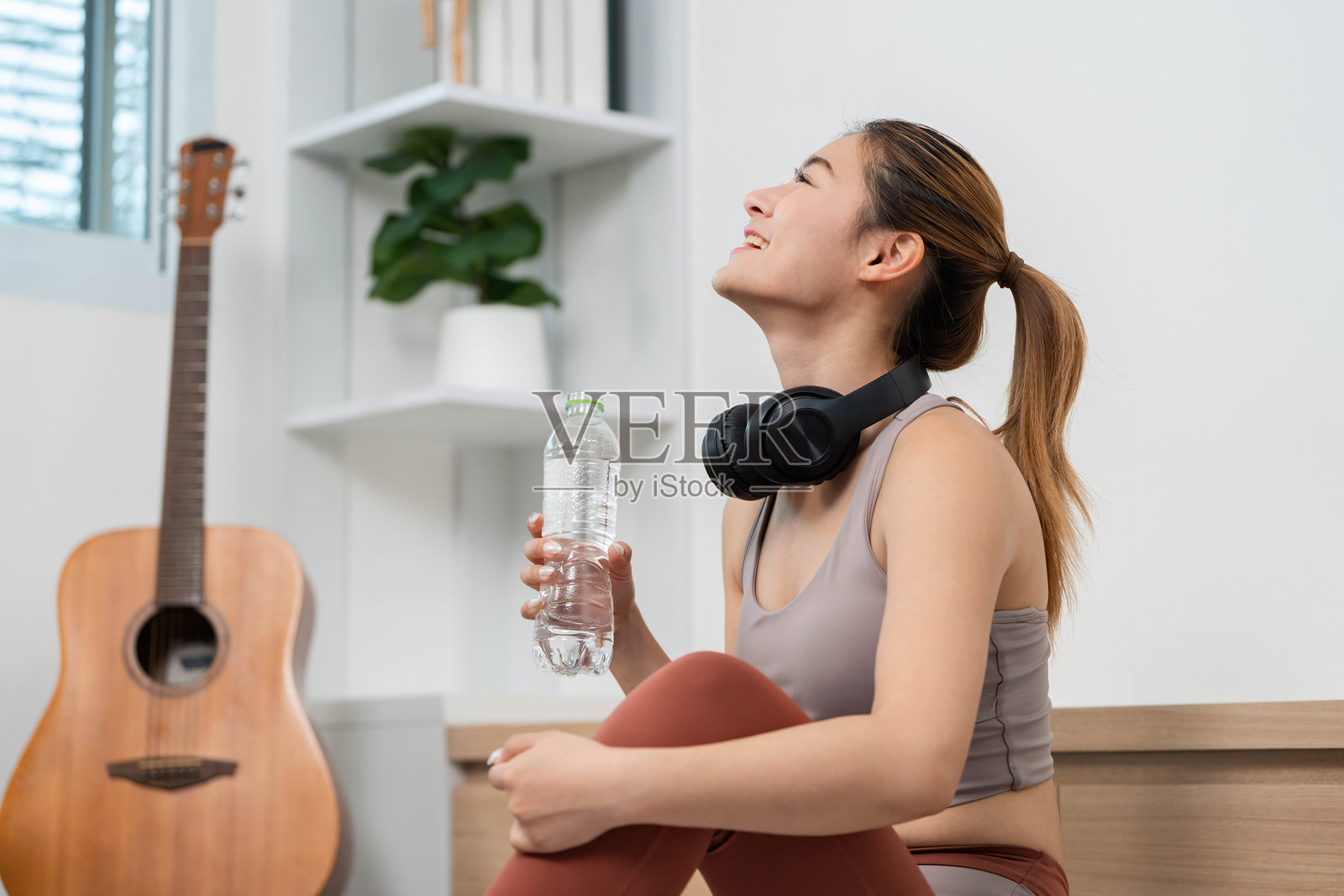 补水与恢复。微笑的女性在舒适的家居环境中享受瑜伽课后的水。照片摄影图片