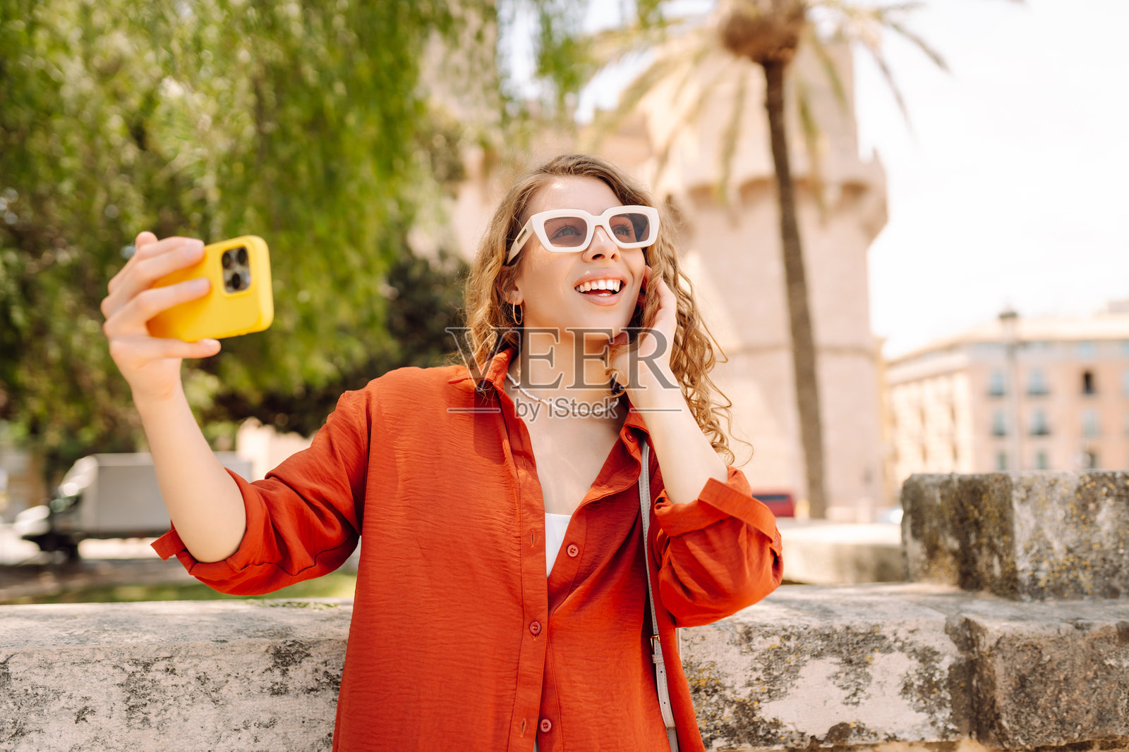 阳光明媚的城市老街背景下，戴着帽子的快乐女性自拍。照片摄影图片