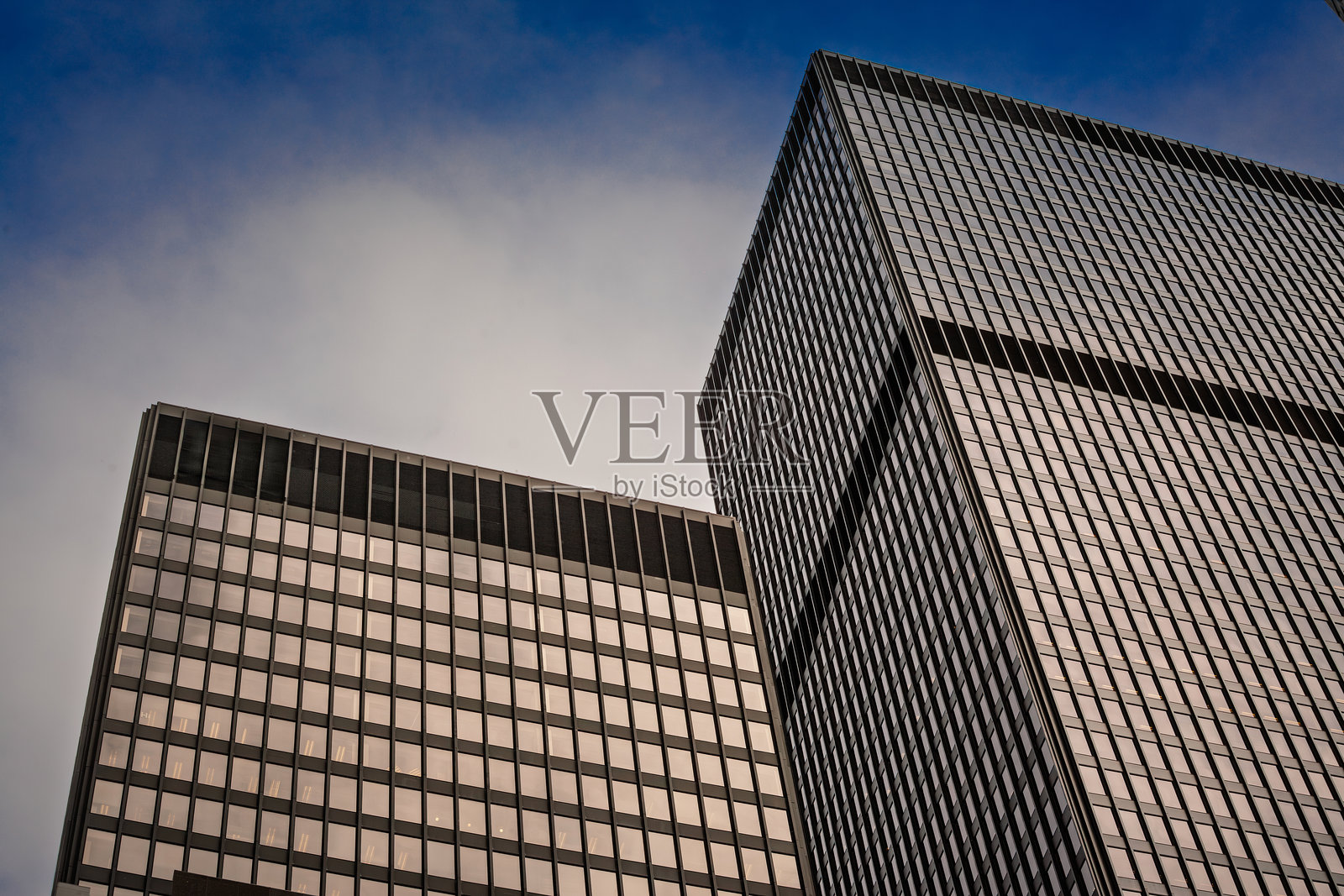 从下方仰视两座位于北美中央商务区的黑色玻璃钢结构办公大楼，简约的网格外立面在清澈的黄昏光线下显得格外引人注目，传达出企业实力与现代主义设计。照片摄影图片