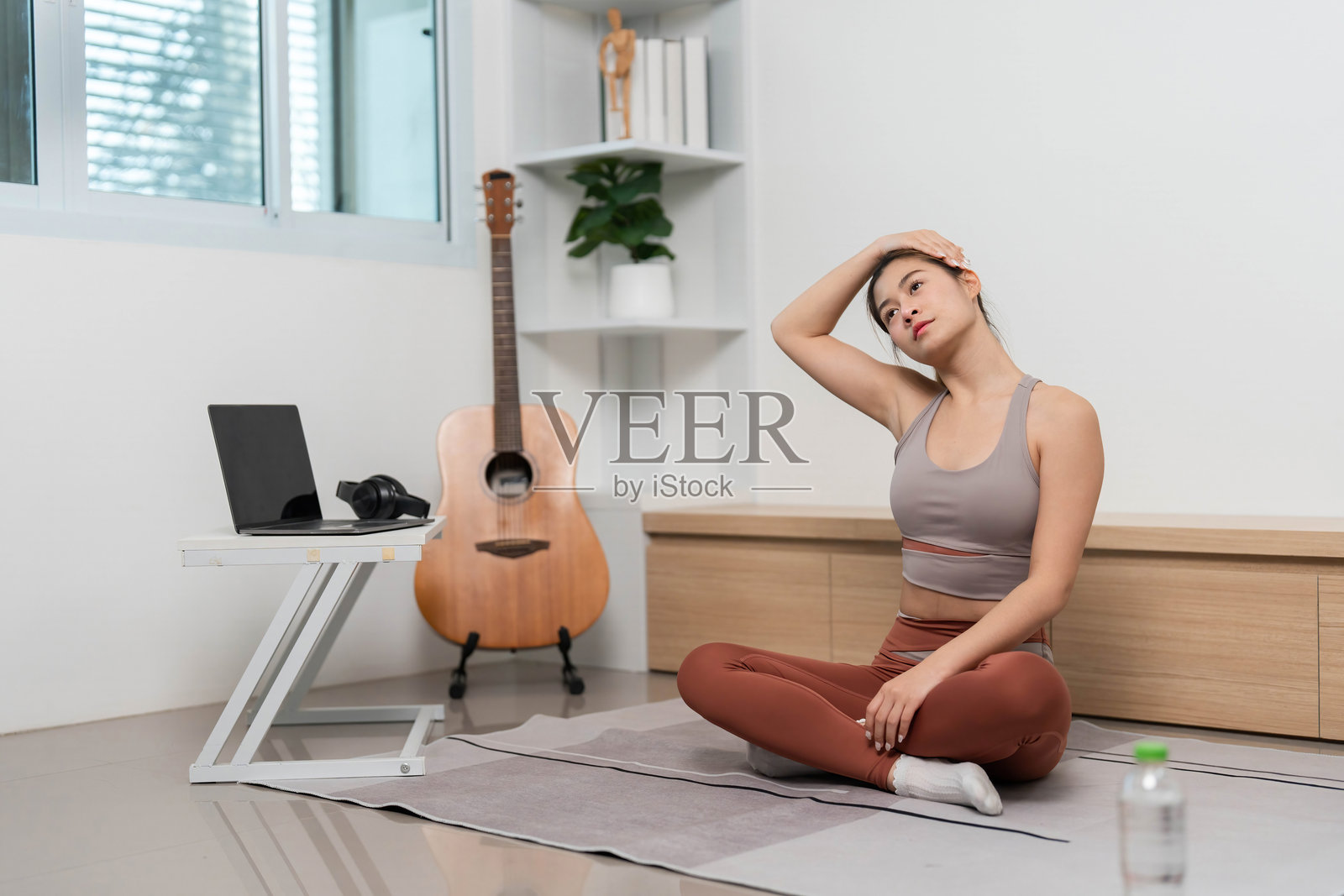 在家练习瑜伽。年轻女性坐在垫子上伸展脖子。照片摄影图片