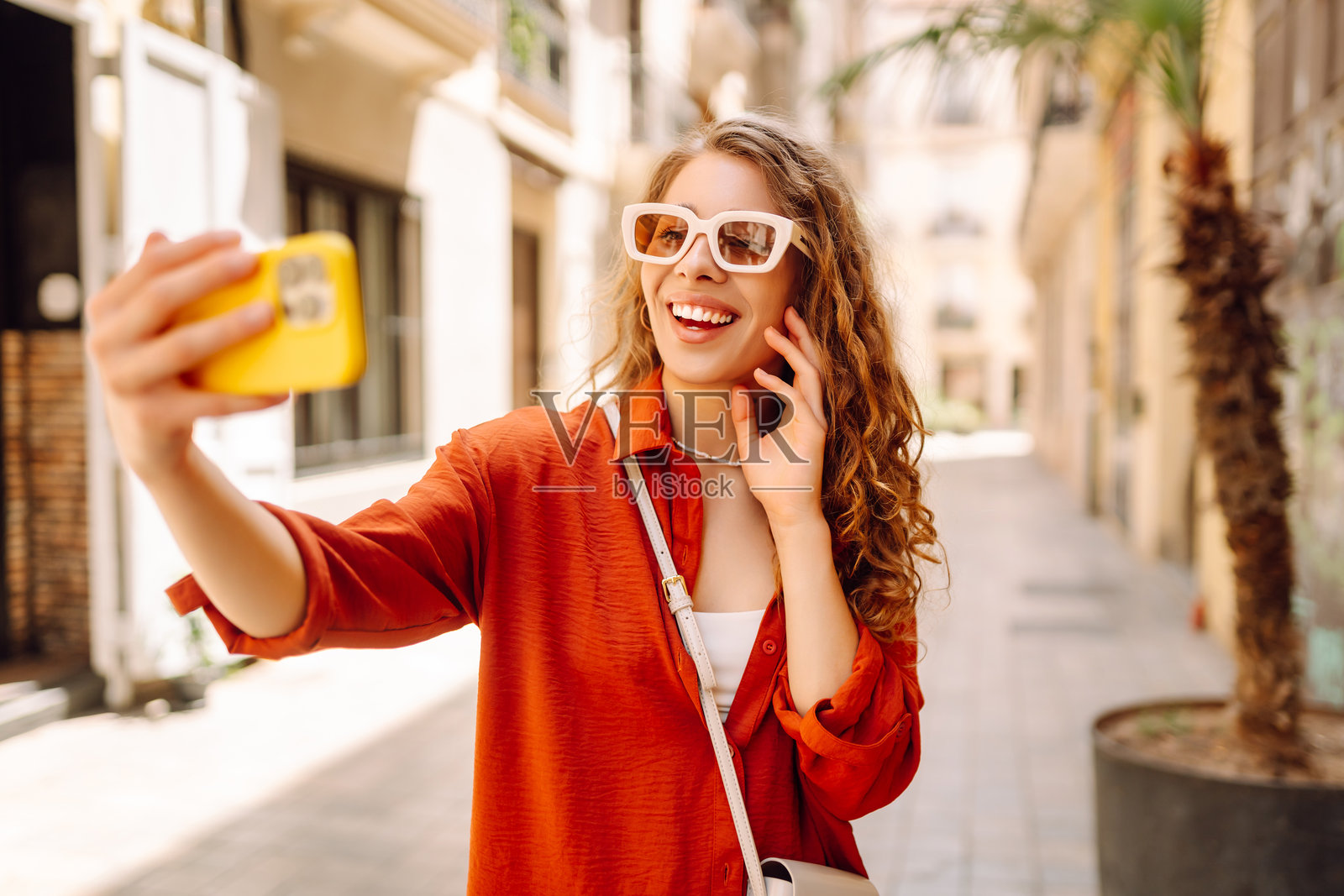 阳光明媚的城市老街背景下，戴着帽子的快乐女性自拍。照片摄影图片