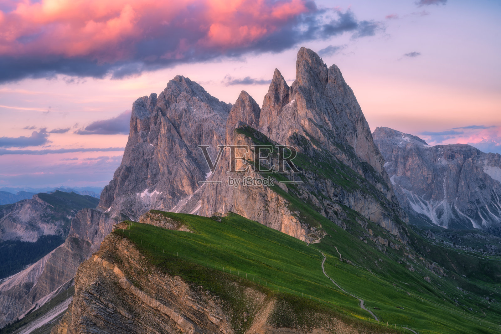 意大利多洛米蒂山脉的塞切达山在夏季美丽的日落时分。色彩斑斓的风景，红色的山峰、岩石、高山草甸、小径、绿色的草地，黄昏时分的粉色天空与云彩。阿尔卑斯山。自然。照片摄影图片