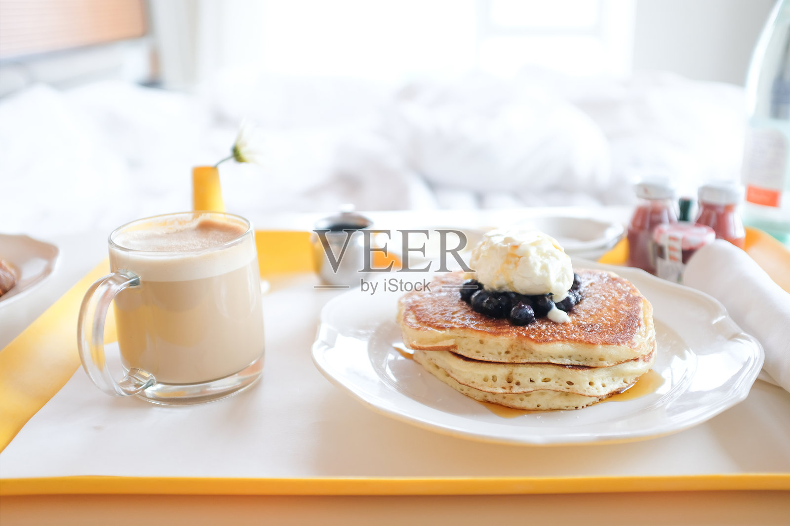房间服务托盘，上面有煎饼和卡布奇诺，背景是床。照片摄影图片