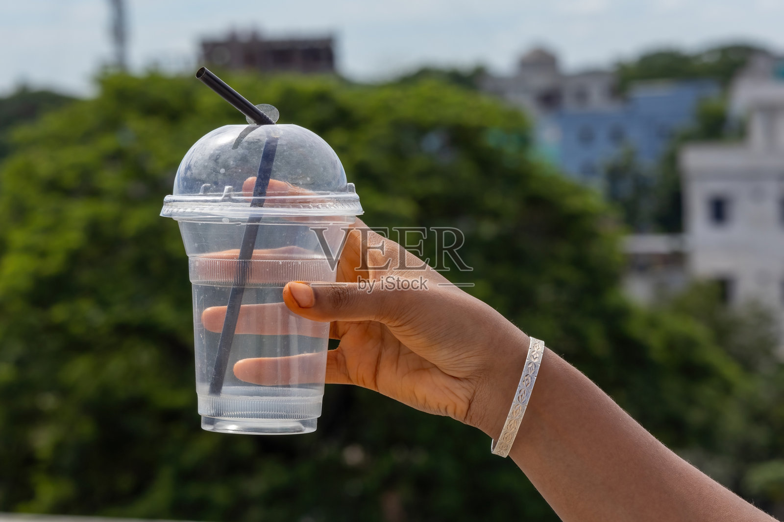女性手握着透明的一次性塑料杯，配有圆顶盖和黑色吸管。非常适合果汁、冷饮或外带饮料。照片摄影图片