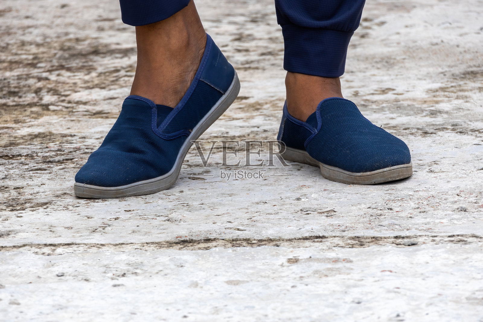 男人穿着海军蓝运动鞋的脚特写，脚踩在混凝土上。舒适时尚的运动鞋。照片摄影图片