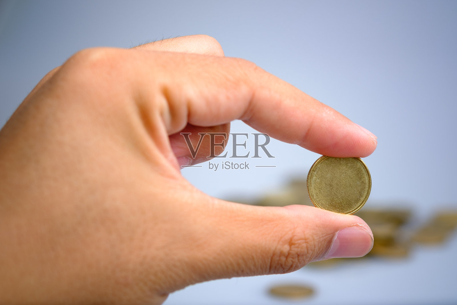 一只手握着一枚没有标签的金色硬币，背景模糊为灰色。照片摄影图片