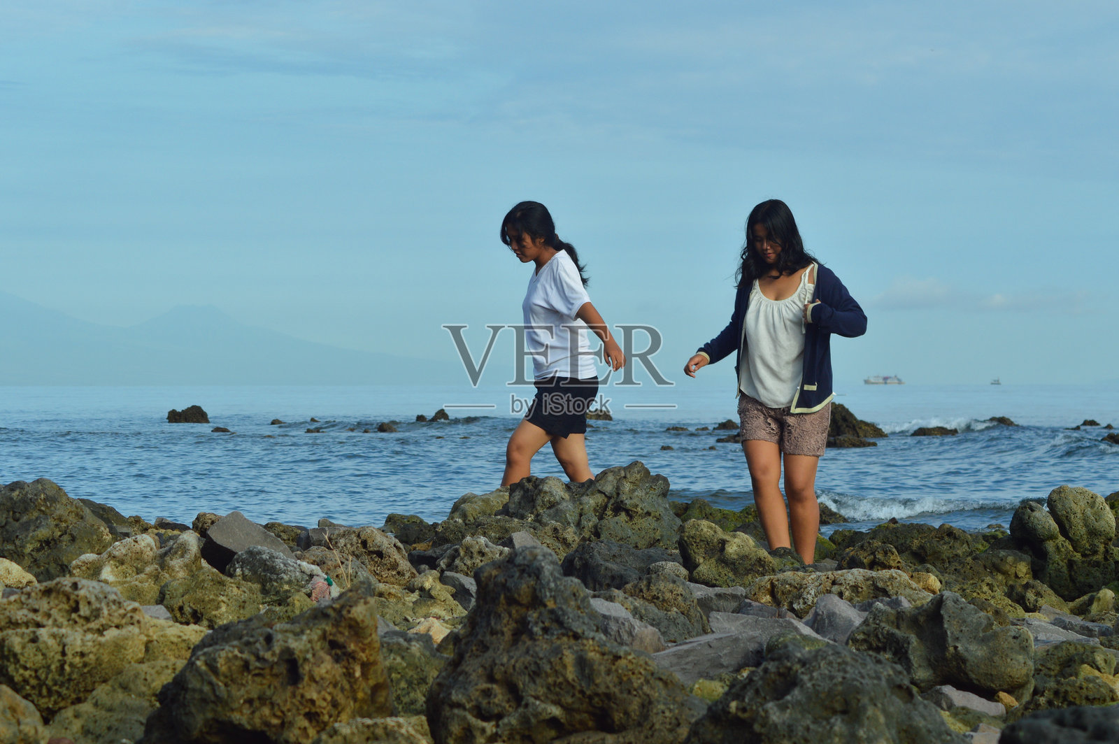 女孩们在海边走过不平的珊瑚岩石照片摄影图片