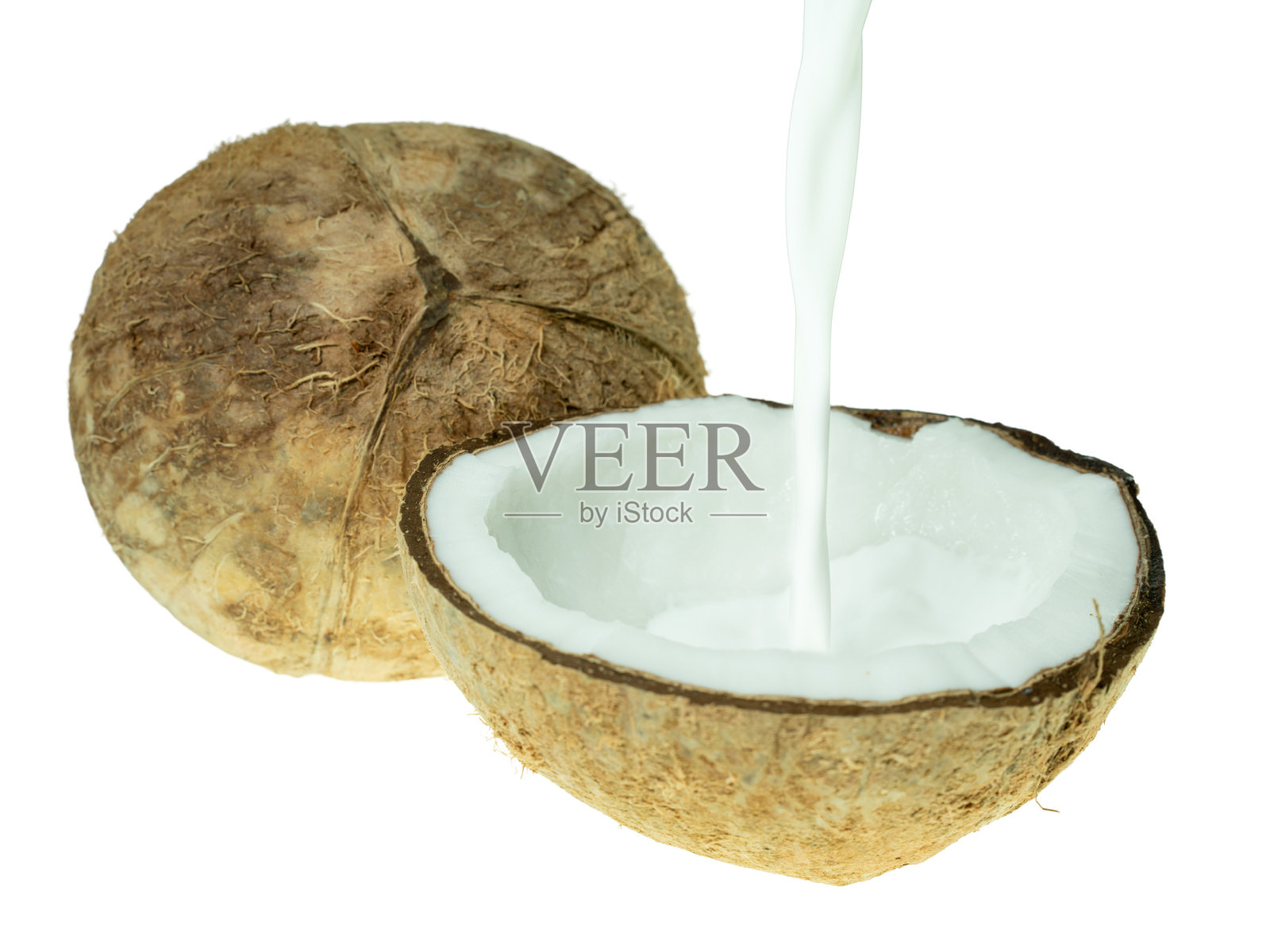 新鲜椰子奶被倒入切开的椰子壳中，背景为白色。热带美食、植物性奶和有机食品成分的概念。照片摄影图片