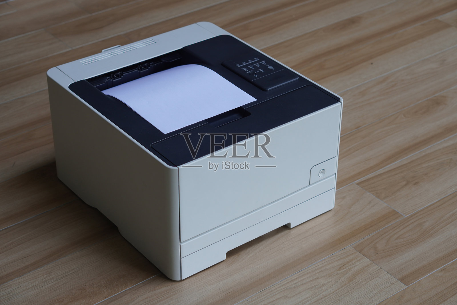 一台紧凑型打印机放在木质地板上，顶部输出槽中露出一张纸。照片摄影图片
