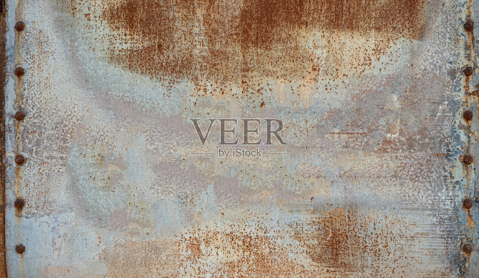 一个严重生锈和受损的蓝灰色金属表面，带有明显的铆钉，形成了工业质感。照片摄影图片