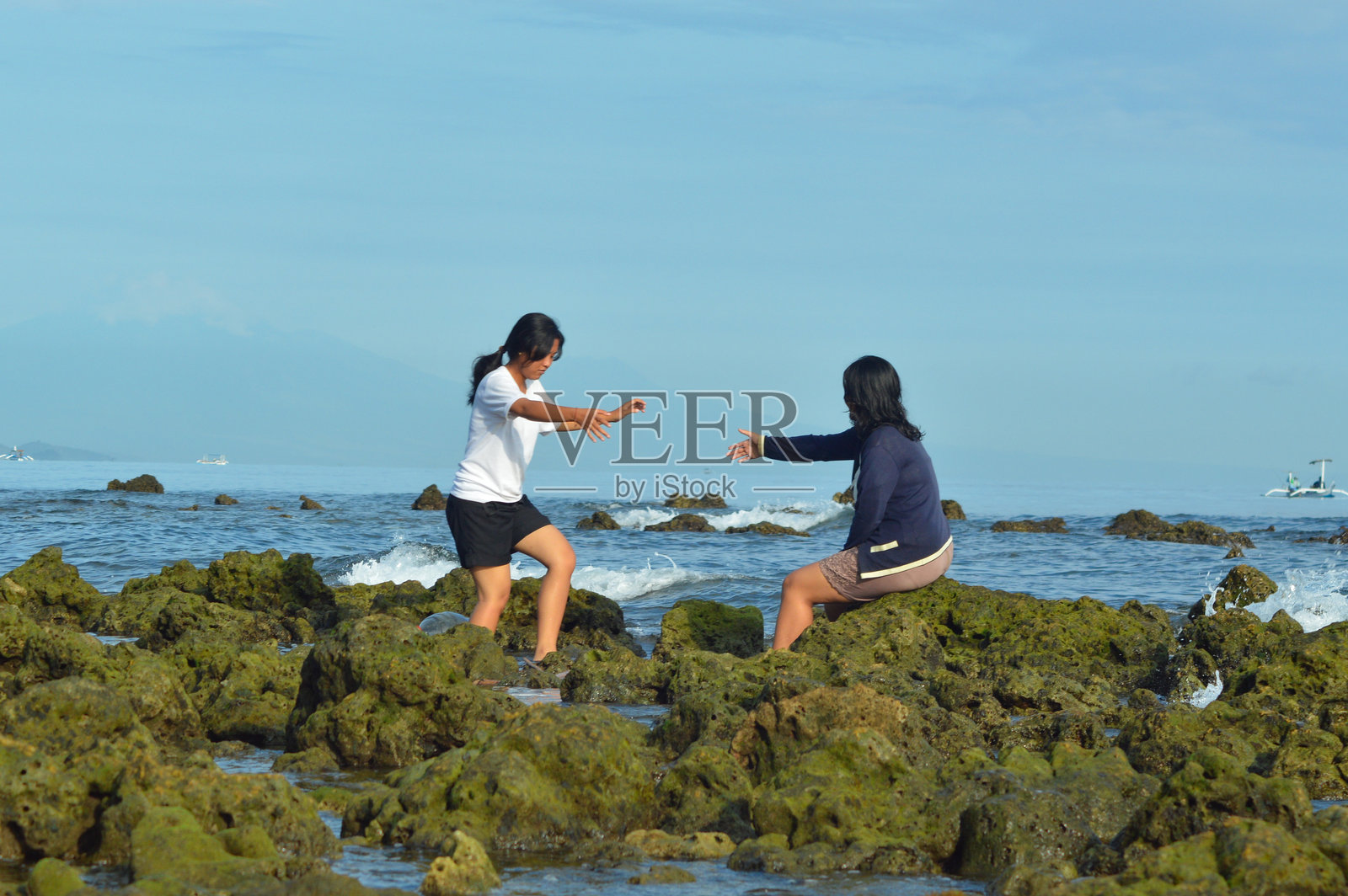 女孩伸出手帮助朋友从海石上站起来照片摄影图片
