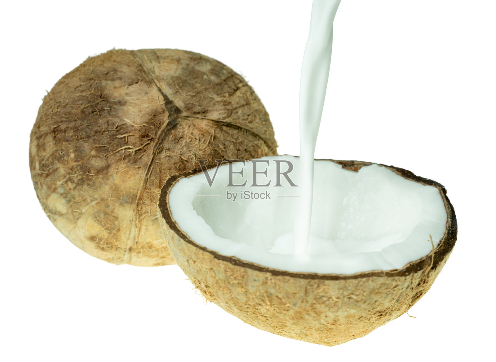 新鲜椰子奶被倒入切开的椰子壳中，背景为白色。热带美食、植物性奶和有机食品成分的概念。照片摄影图片