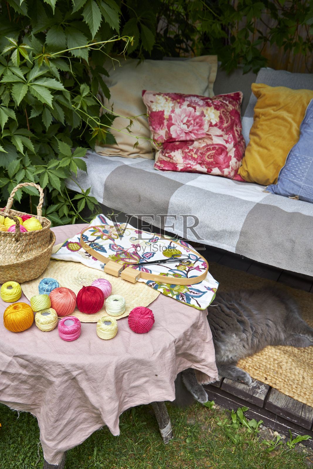 温暖的夏日里，小花园桌子的特写，桌上摆放着刺绣用品。五彩缤纷的线、针、布料、剪刀和木环在自然光下整齐地排列。桌子位于盛开的花园中，营造出一个舒适而富有灵感的户外环境。照片摄影图片
