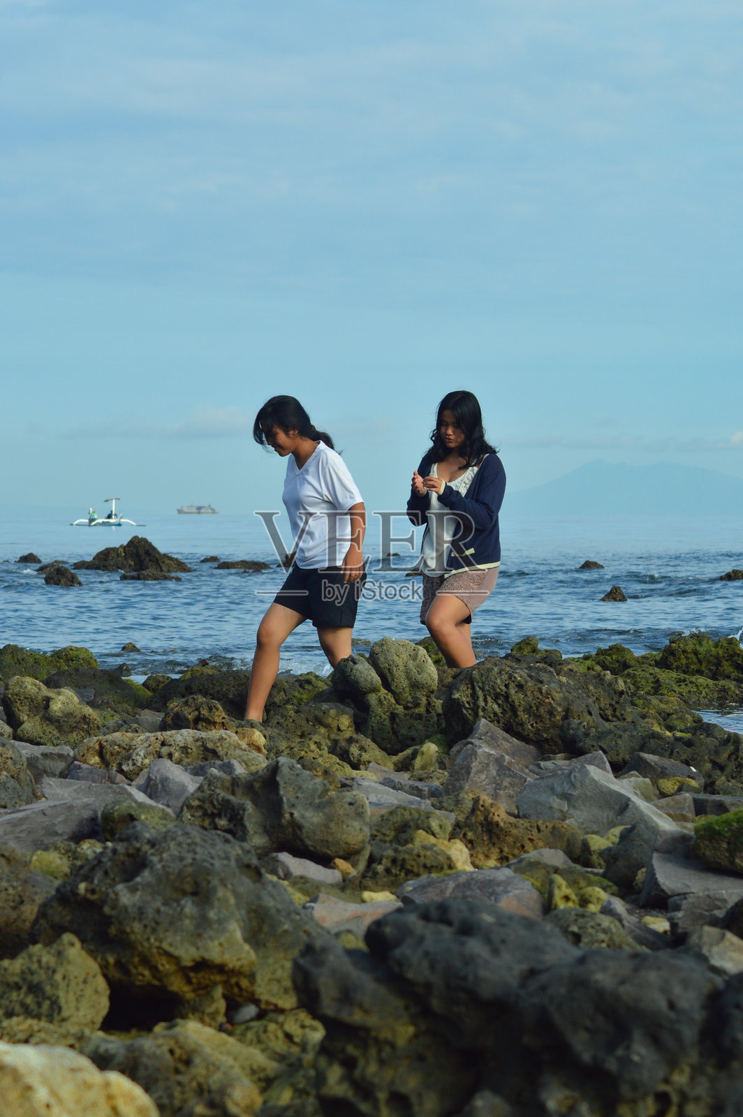 女孩们在海边的岩石间走路，低头看着地面。照片摄影图片