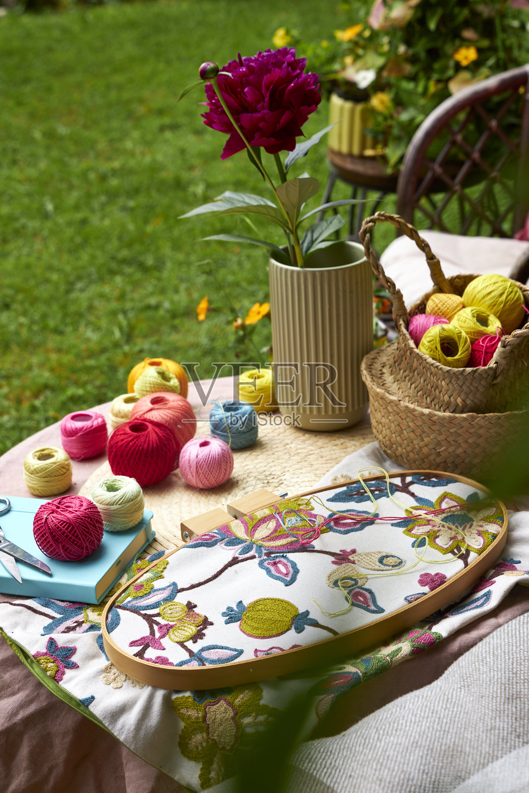 温暖的夏日里，小花园桌子的特写，桌上摆放着刺绣用品。五彩缤纷的线、针、布料、剪刀和木圈在自然光下整齐地排列着。桌子位于盛开的花园中，营造出一个舒适而富有灵感的户外环境。照片摄影图片