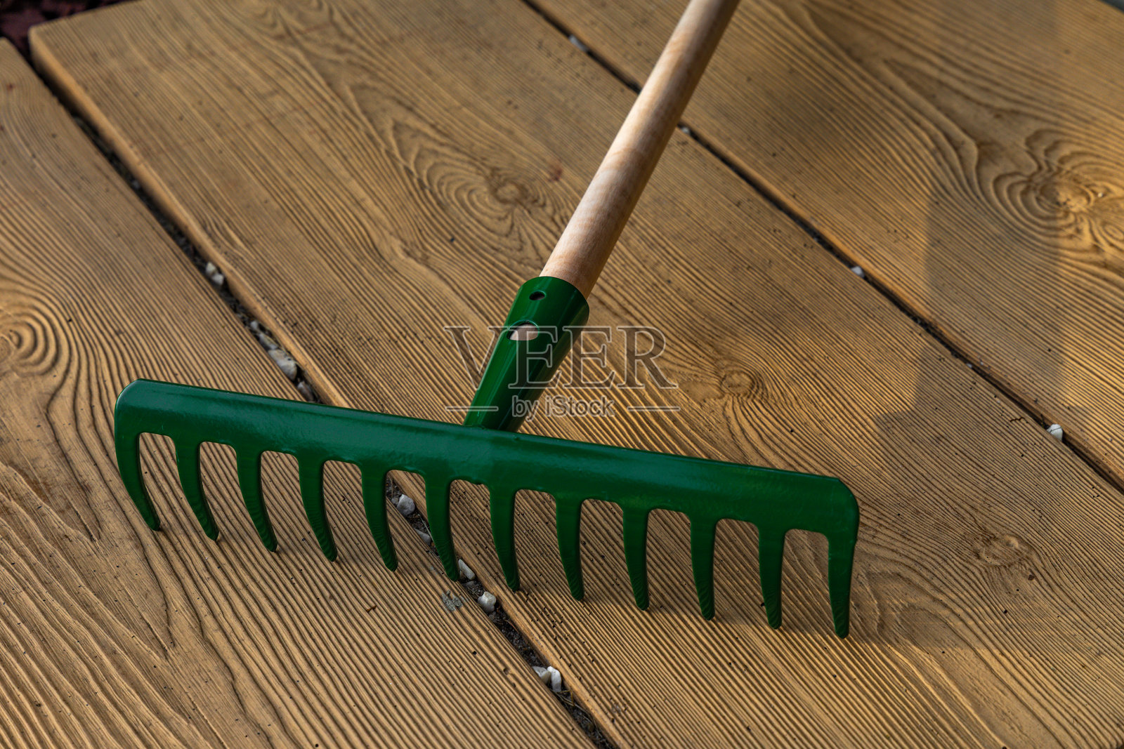 新绿色的耙子放在入口前的瓷砖上，用于耙叶子。照片摄影图片