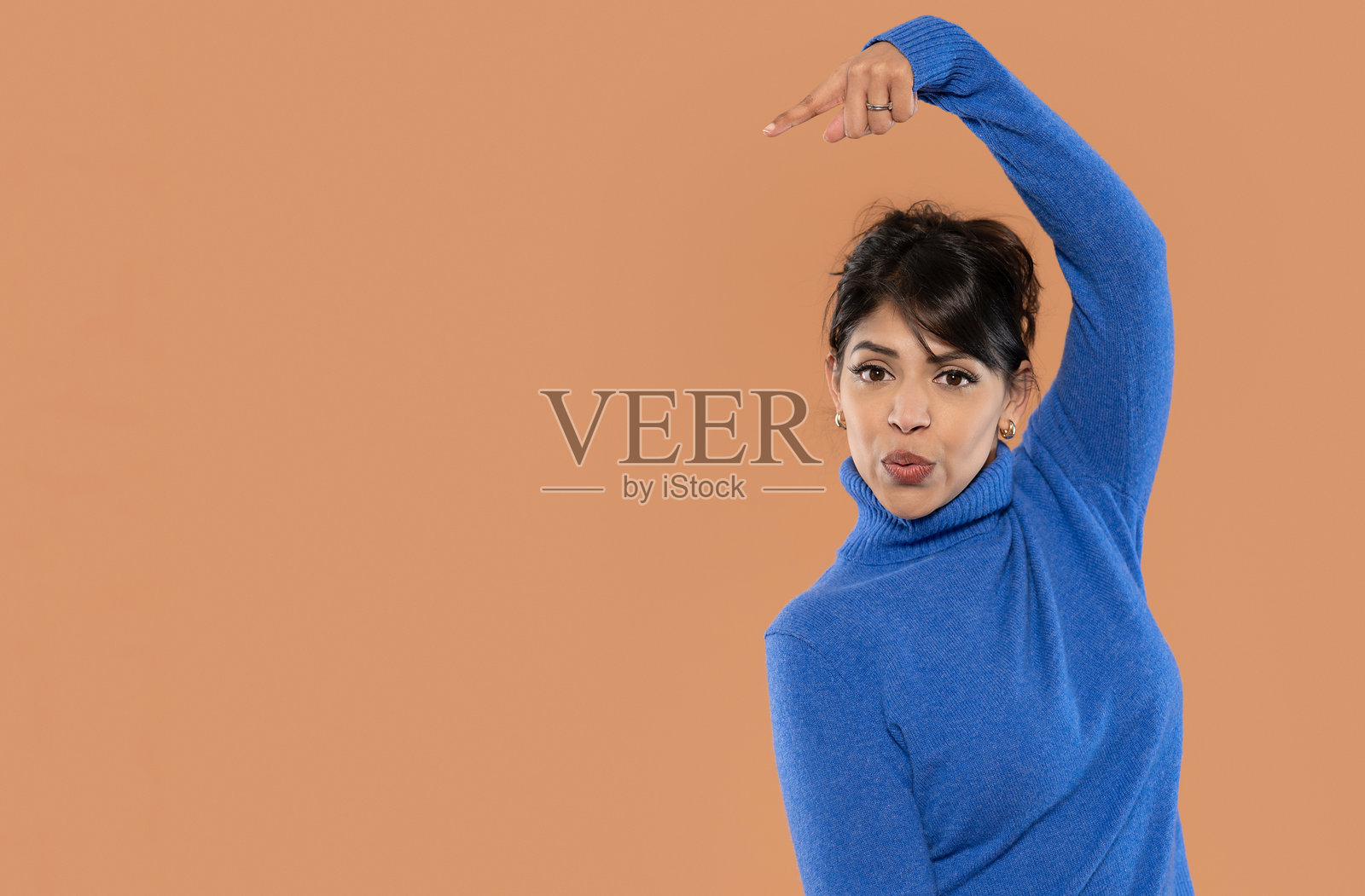 穿着蓝色毛衣的女性在棕色背景前俏皮地摆姿势，享受着她的时光，展现出她的兴奋和魅力。照片摄影图片