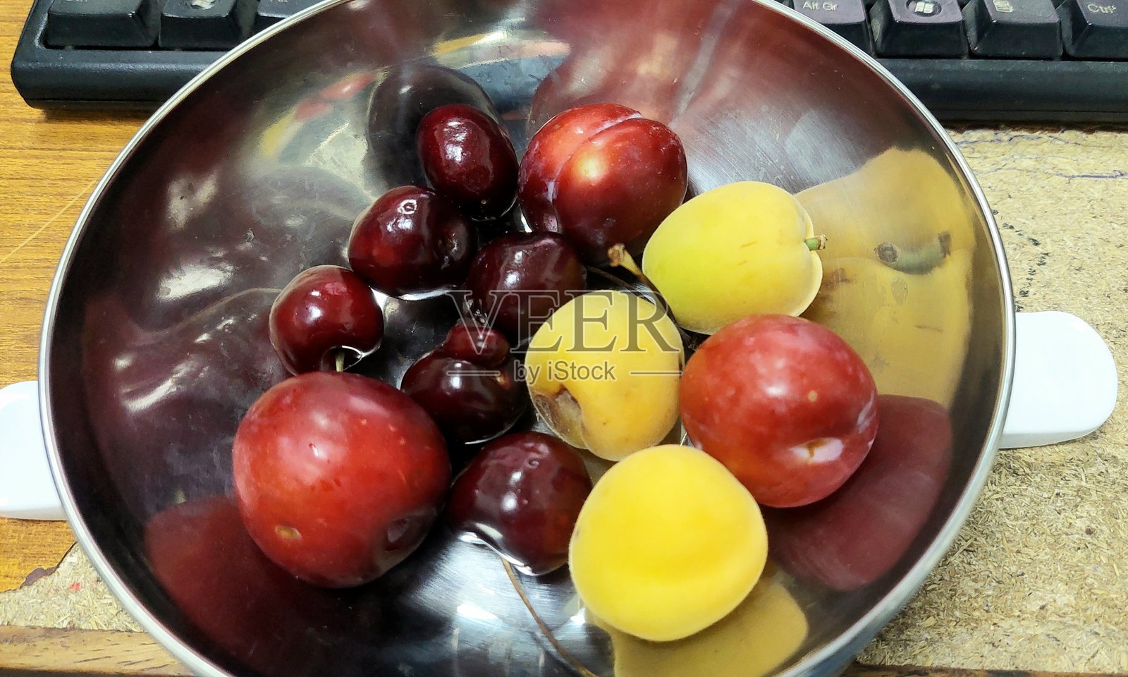 特写镜头展示了一个钢碗中的杏子、李子（阿洛布哈拉）和一种独特的变异樱桃，突显夏季的清新和自然的多样性。照片摄影图片