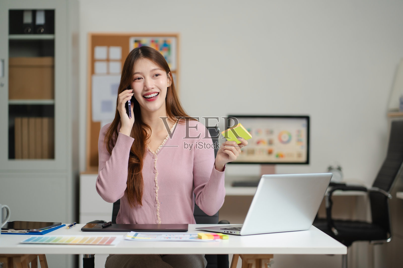 女性程序员或开发者在工作场所通过手机与电脑屏幕进行问题解决。照片摄影图片
