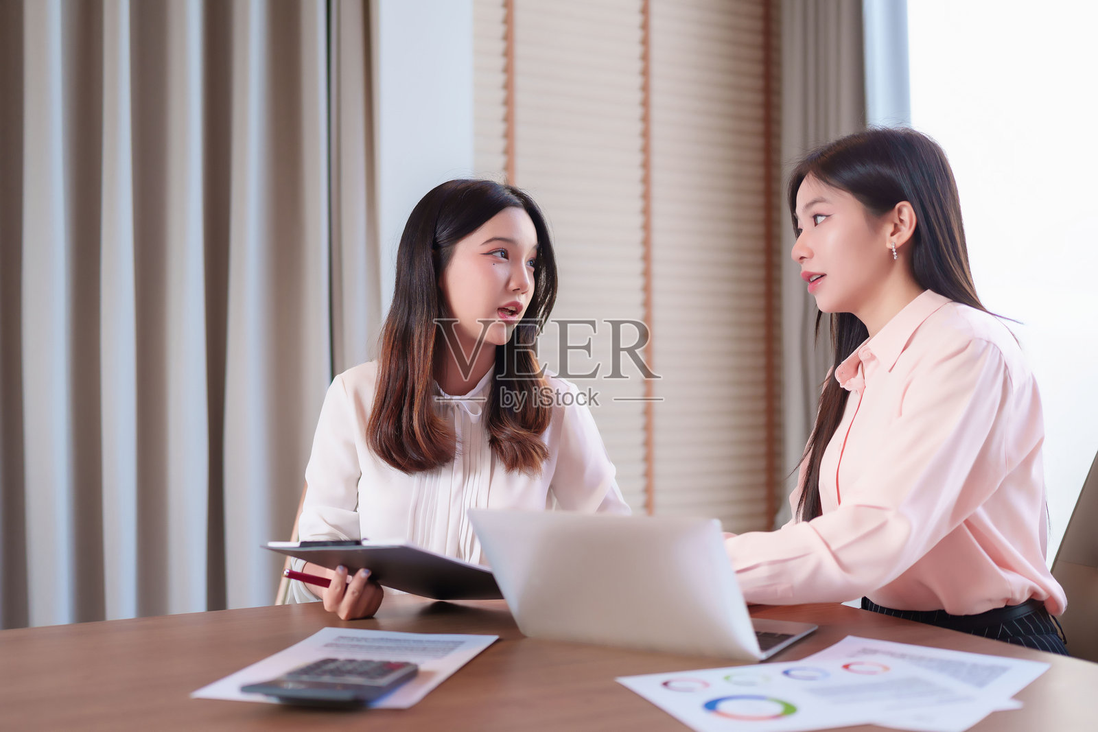 亚洲女性在办公室会议室讨论商业策略，成年专业人士分析数据，使用笔记本电脑和夹子，现代职场合作。照片摄影图片