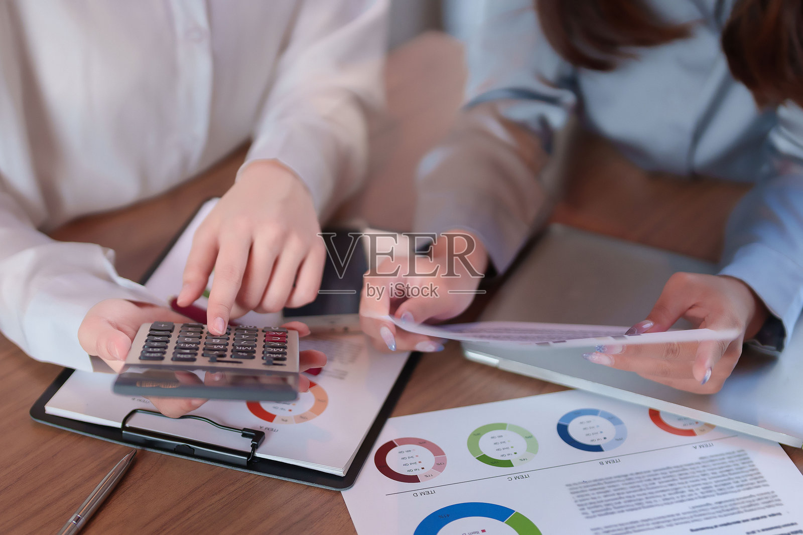 亚洲成年女性在会议中使用计算器分析财务数据，桌上有会计预算报告、统计数据和图表。照片摄影图片