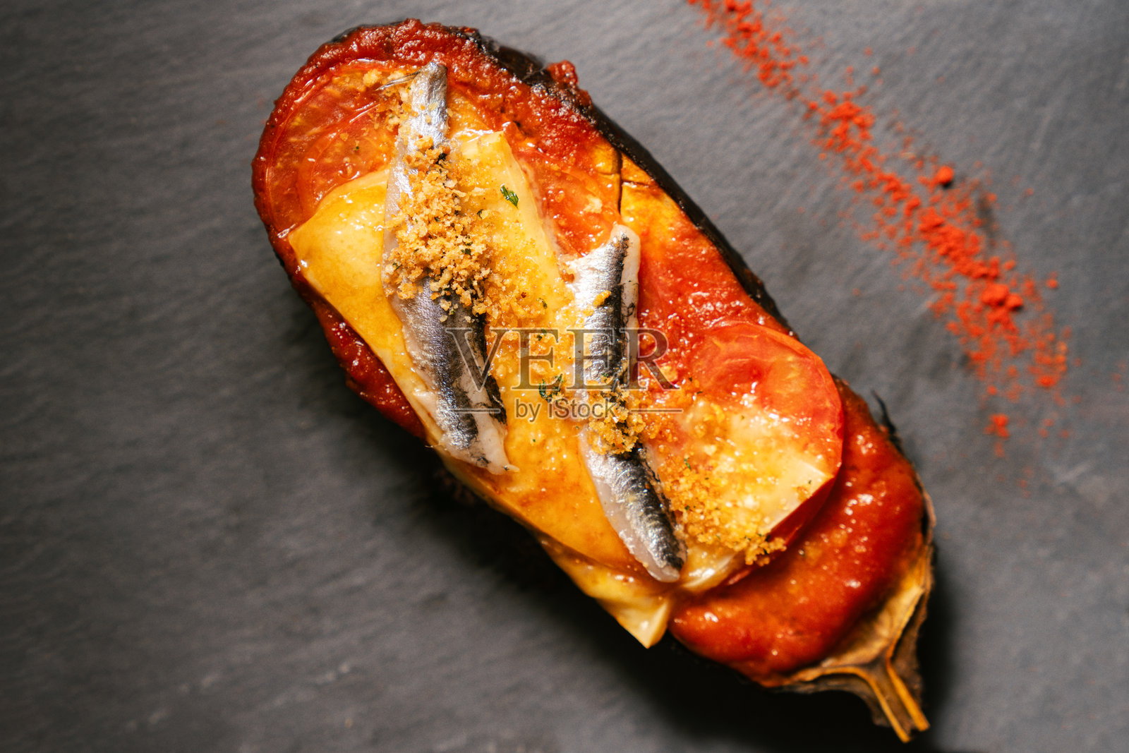 烤茄子配番茄酱、奶酪、凤尾鱼和面包屑，背景为石板照片摄影图片