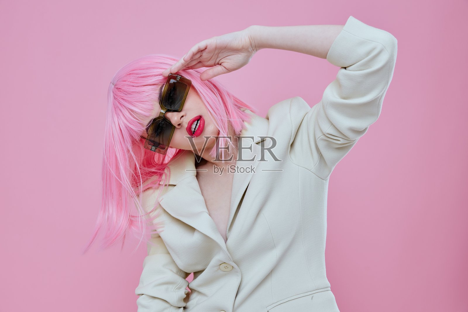 年轻女性戴着太阳镜，粉色头发，摆姿势于彩色背景前照片摄影图片