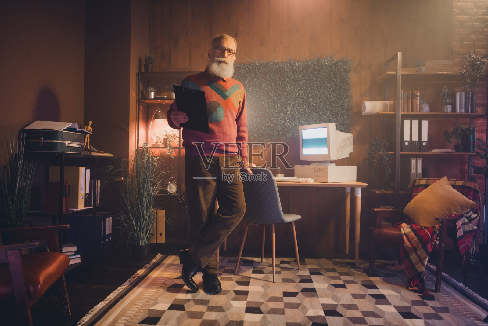 成熟男性在舒适的家庭办公室环境中使用复古电脑，周围环绕着温馨的装饰和复古设备。照片摄影图片