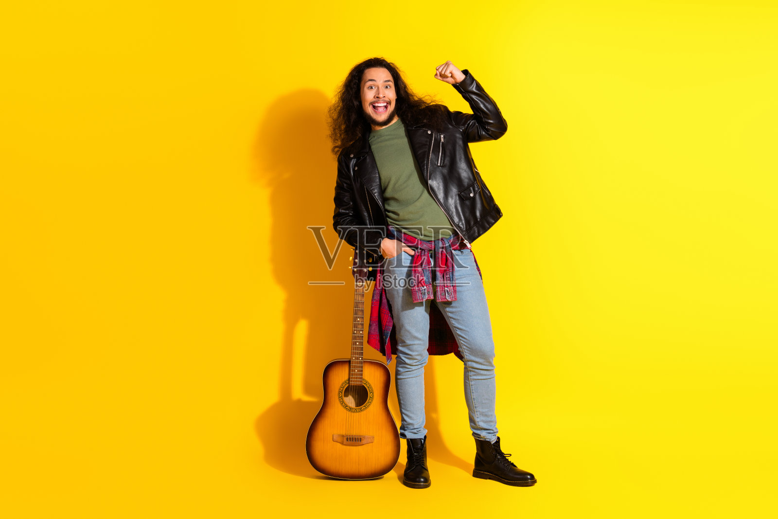 阳光开朗的年轻男子在明亮的黄色背景前摆姿势，手持原声吉他，散发出时尚和有趣的休闲氛围。照片摄影图片